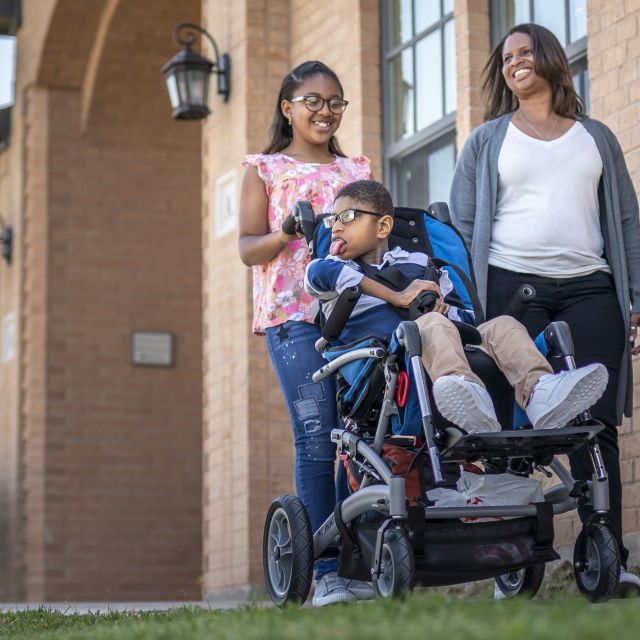 Two women, and a young man in a wheelchair out for a walk in front of a building