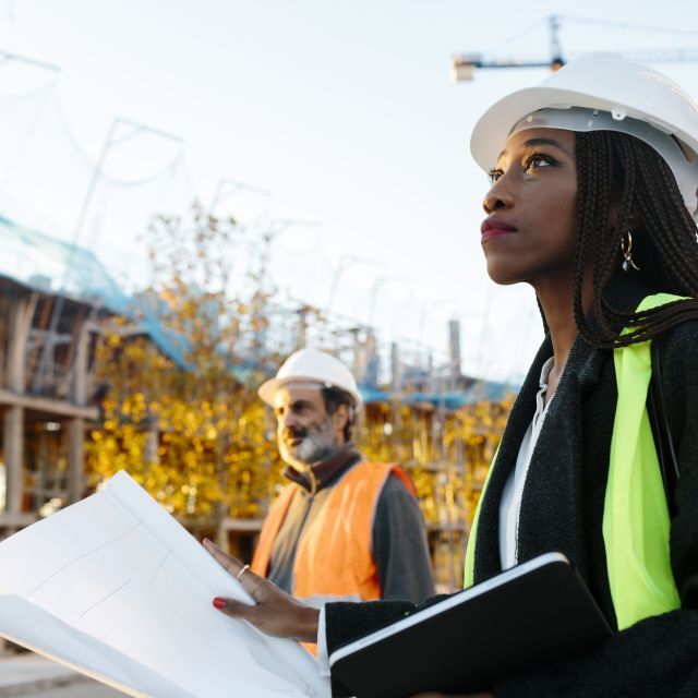 Black woman holding construction plans at a construction site during build