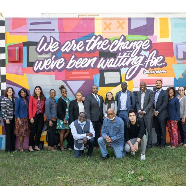 A group of people in front of a mural with a quote "We are the change we've been waiting for"