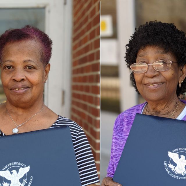 Carlise Jones and Pearl Wilson holding blue folders with The President's Lifetime Achievement Award imprinted