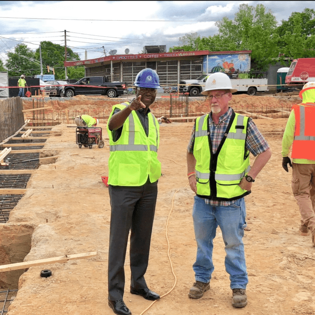 Two men standing on a construction site talking while a third person is walking in the background