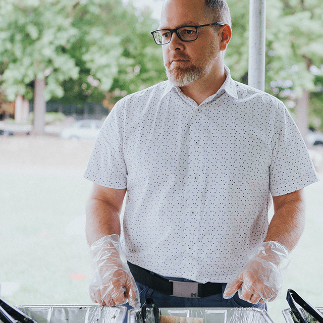 A man in a white shirt serving food with plastic gloves on