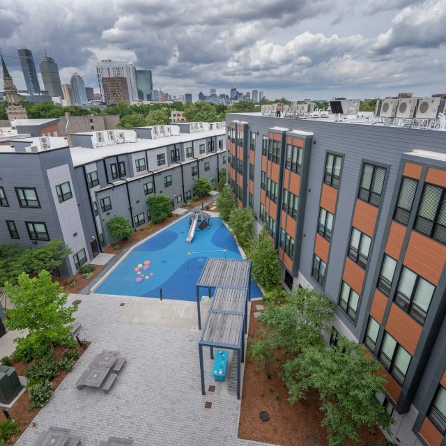 Rooftop view of multifamily housing development with a courtyard, playground, and a blue sky and white puffy clouds overhead 