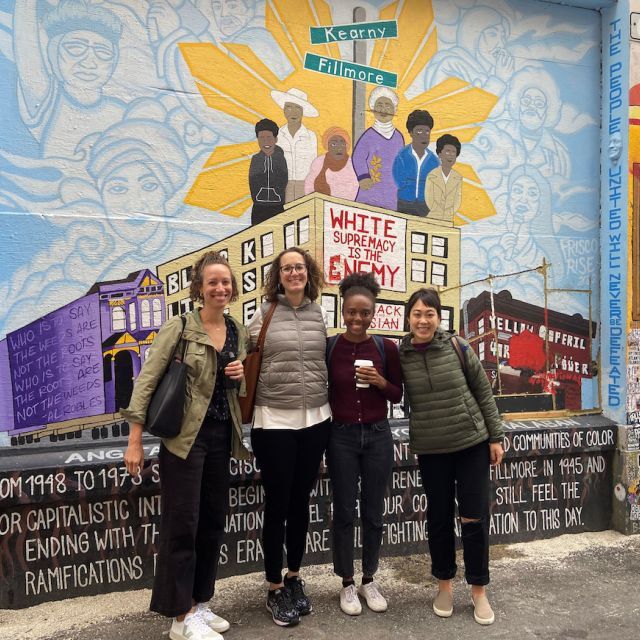 Photo of four women in front of colorful mural