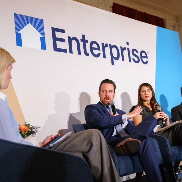 Panelists speaking on a stage with the word Enterprise on the wall behind them