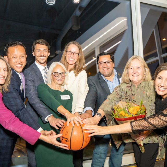Photo of People Standing in a Semi-Circle With Hands on a Basketball