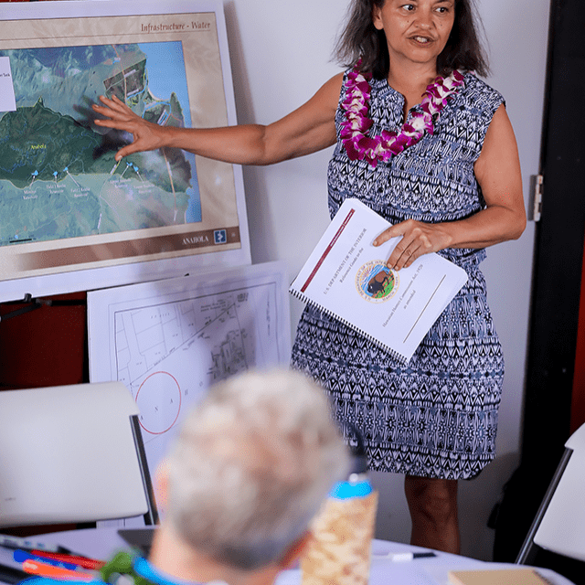 A woman speaking to a group and pointing to a map on an easel