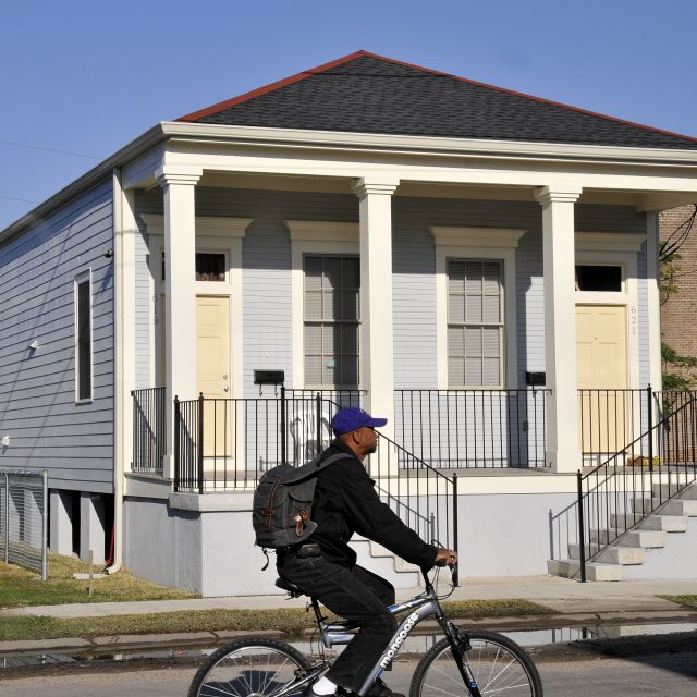 A man riding a bicycle in front of a home