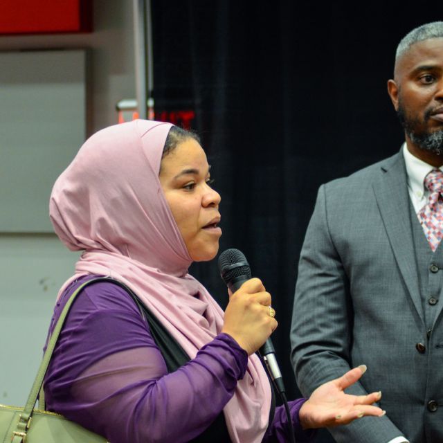 Woman in hijab speaking in microphone with a man standing next to her