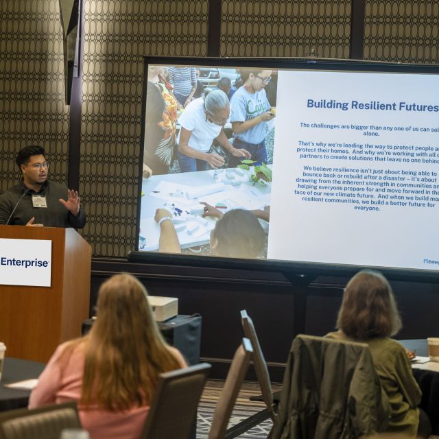 Man speaking at podium before an audience. A large screen next to him reads, "Building Resilient Futures."