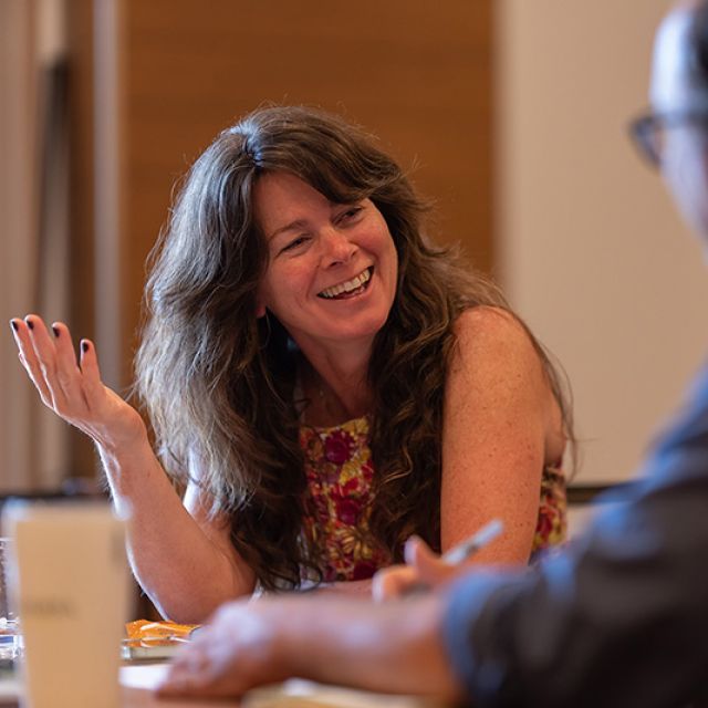 A woman and man sitting at a table talking as the woman smiles and gestures with her hands