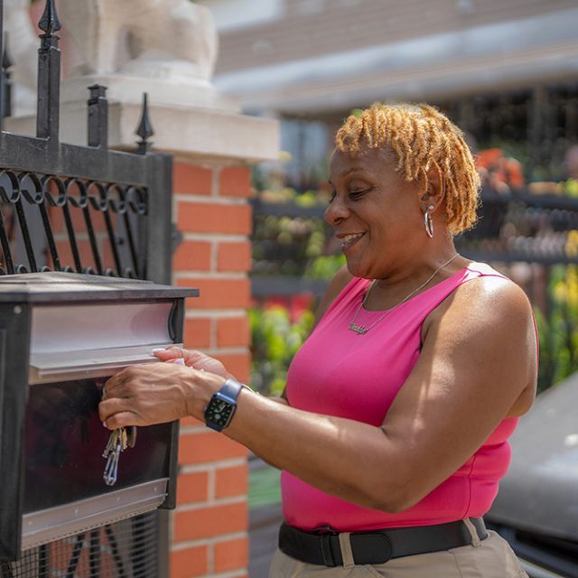 A woman using a key to open a black and silver mailbox