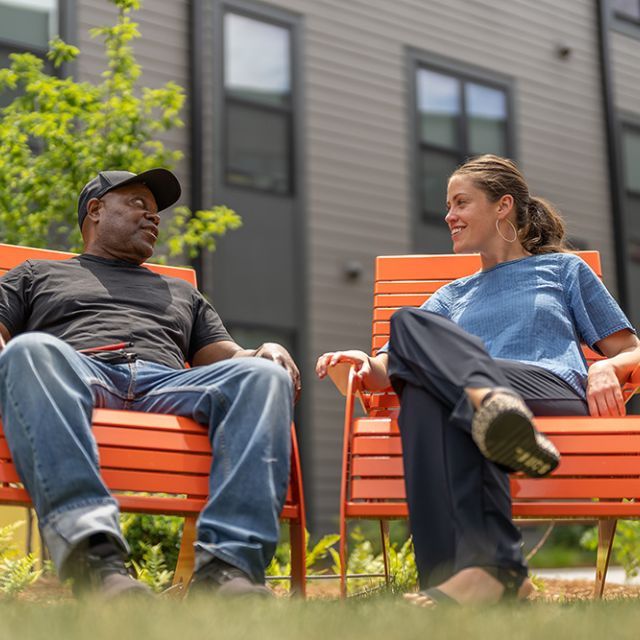 A man and a woman sitting outdoors in orange lawn chairs talking