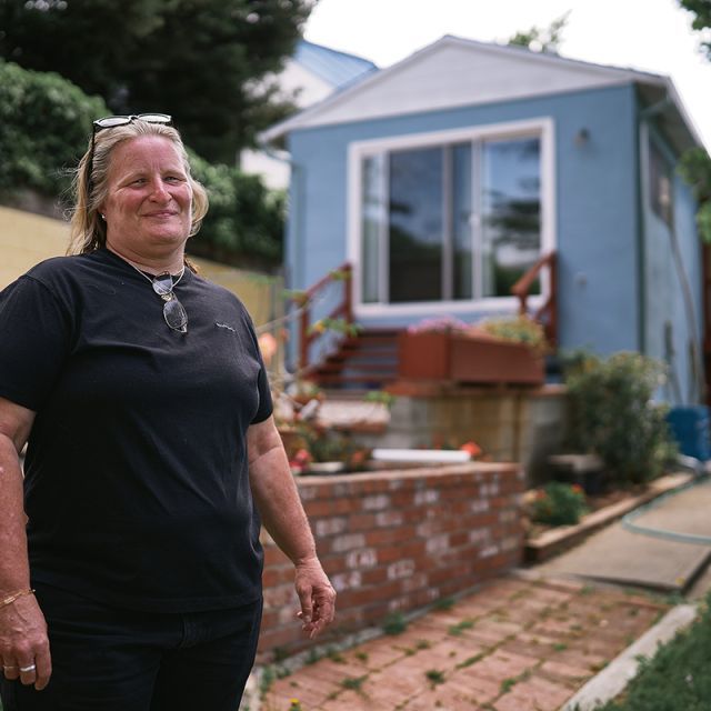 A woman standing in front of a blue home with a red brick walkway