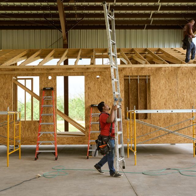 Construction worker carries a ladder in front of a home being built