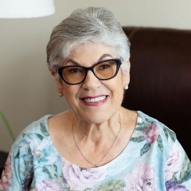 Sharron Morden, Cadence Resident, seated wearing a floral shirt and eyeglasses