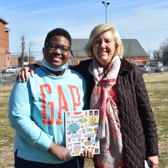 A young mentee and mentor stand at a park with apartment buildings in the background 