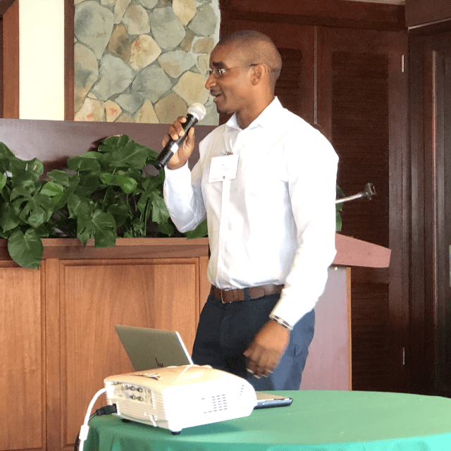 Jelani Newton holds a microphone beside a table with a projector on it