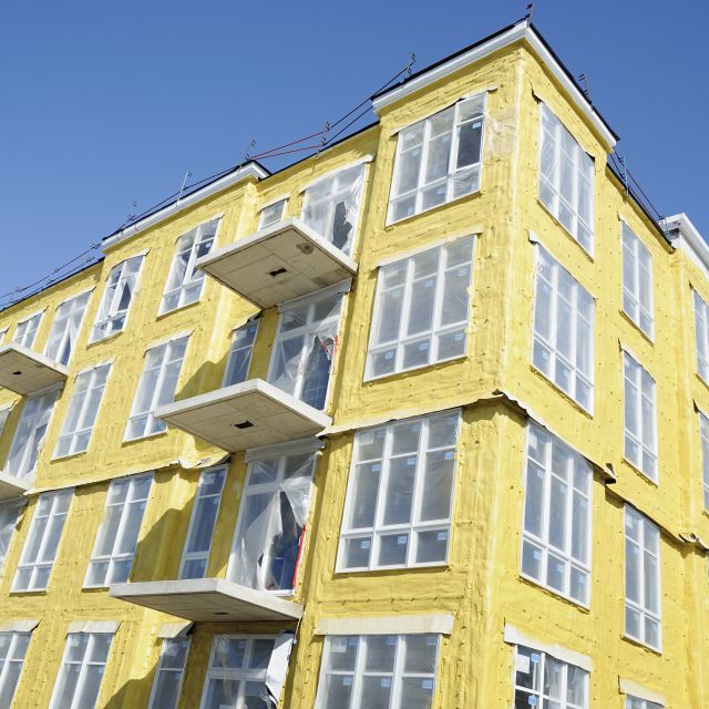 Aspect of a multistory building with yellow insulation and a bright blue sky overhead.