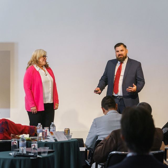 A man and a woman standing on stage presenting to a group of people