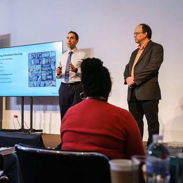 Two people standing in front of a screen presenting to a group