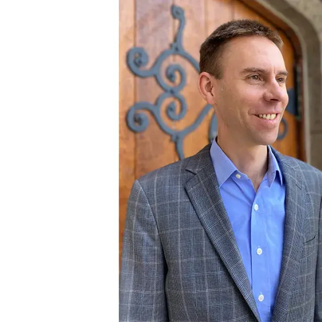 Man stands and smiles in front of a wooden door with a wrought iron pattern