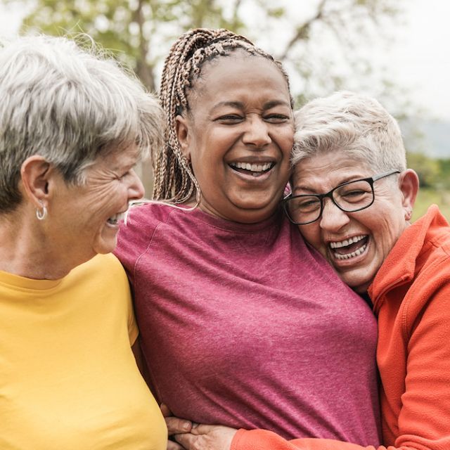 Three women laughing and hugging outside