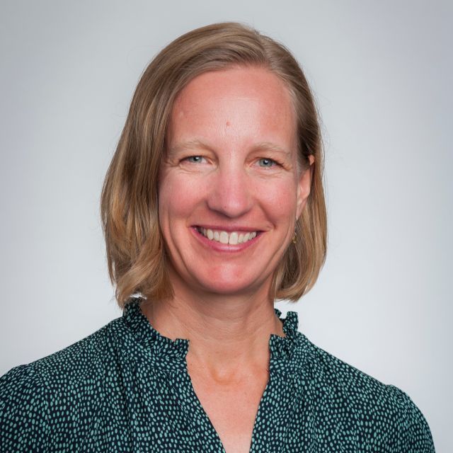 Person smiling with light brown hair and black patterned blouse.