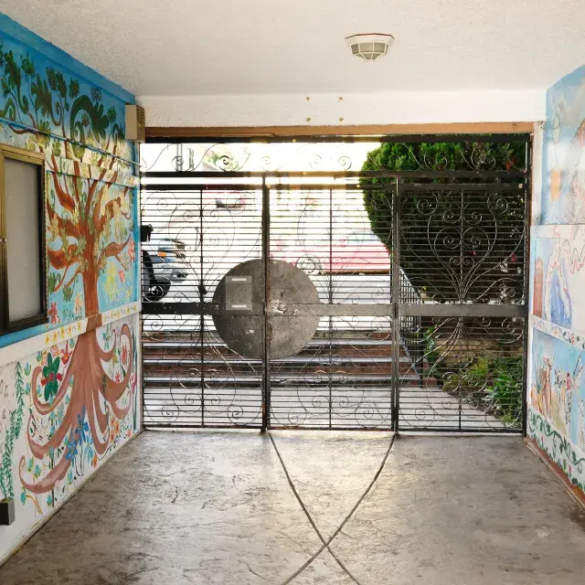 A slotted gated door with a window at the end of a hallway with colorful murals painted on both walls