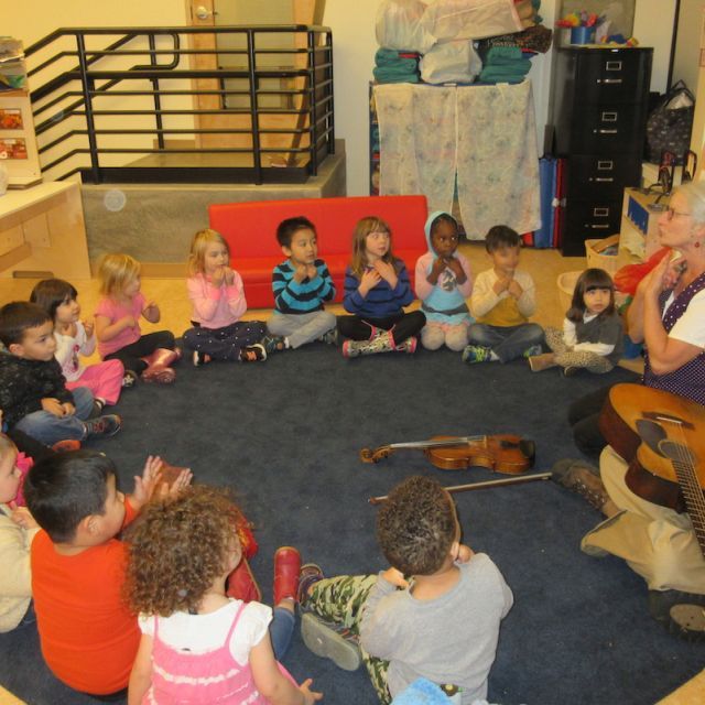 Children sitting on the floor in a circle participating in a music lesson