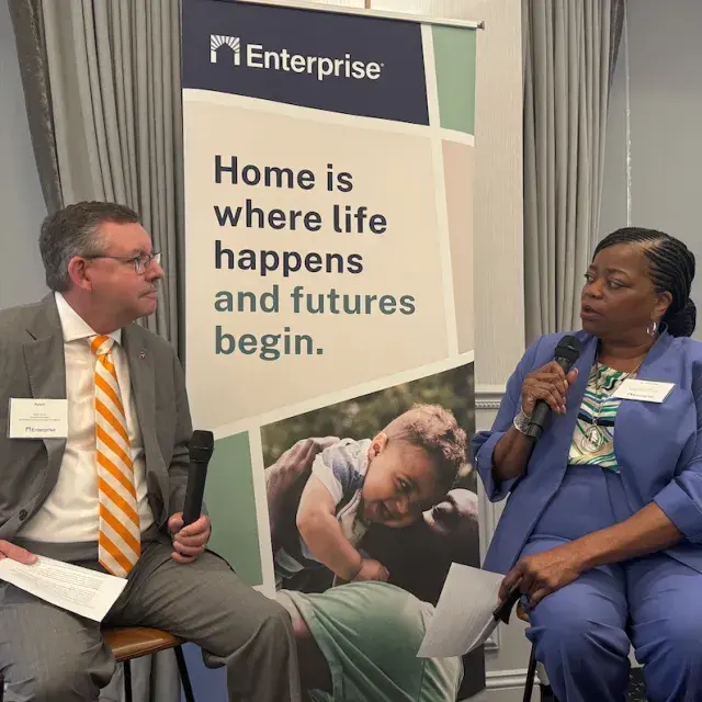 Woman in blue suit interviewing man in grey suit and striped, orange tie.