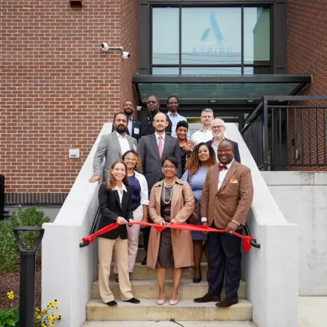 People in business attire standing on a stairway behind a red ribbon. 
