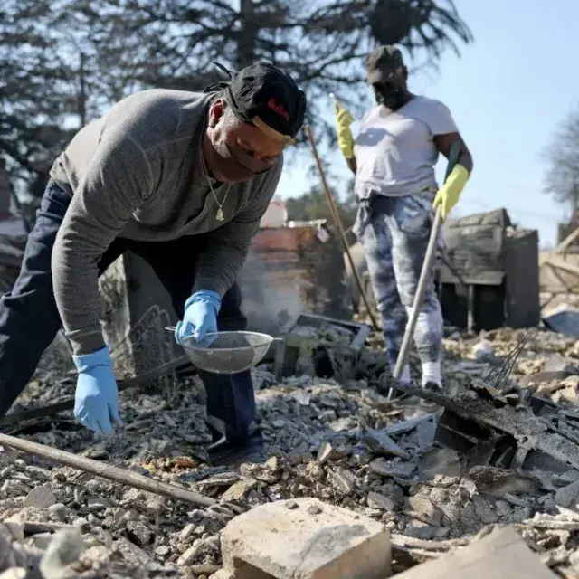People wearing jeans, work shirts, and masks picking through debris after a wildfire