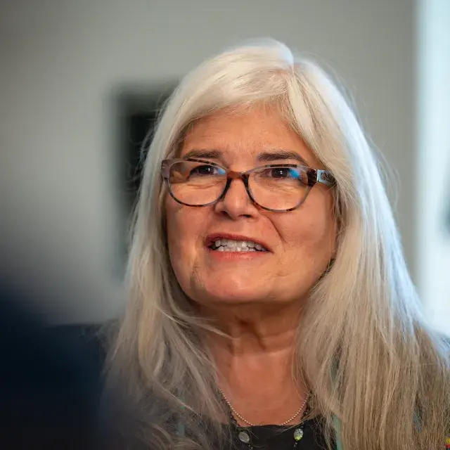 Person with long silver hair wearing glasses looks up, smiling