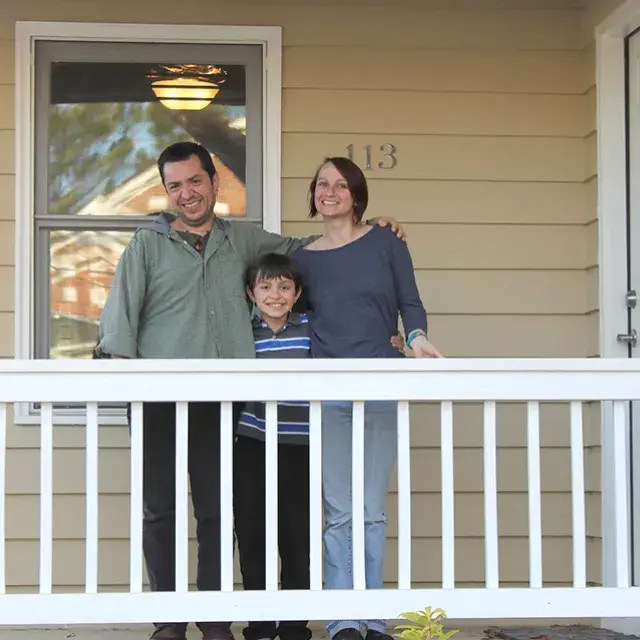 A family of three standing on a the front porch smiling