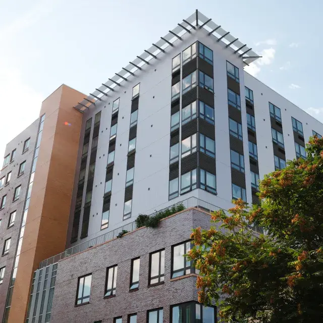 Modern high-rise apartment building flanked by trees and light blue sky 