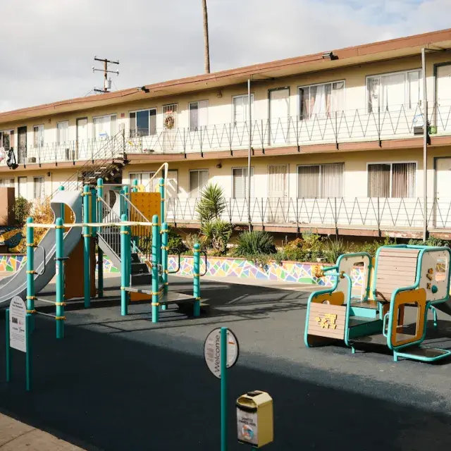 Picture of three-story cream apartment building with playground in foreground