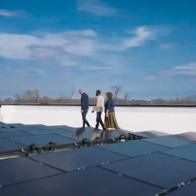 Three people walk alongside a rooftop solar array with a blue sky and clouds in the background