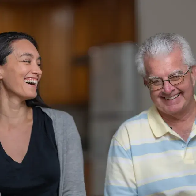 Two people sit side by side smiling and laughing.