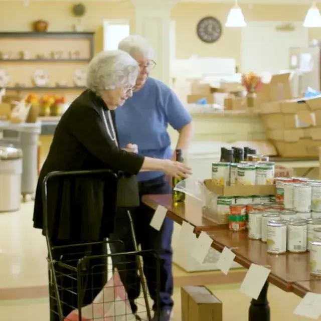 Two women looking at canned and jarred food on table.