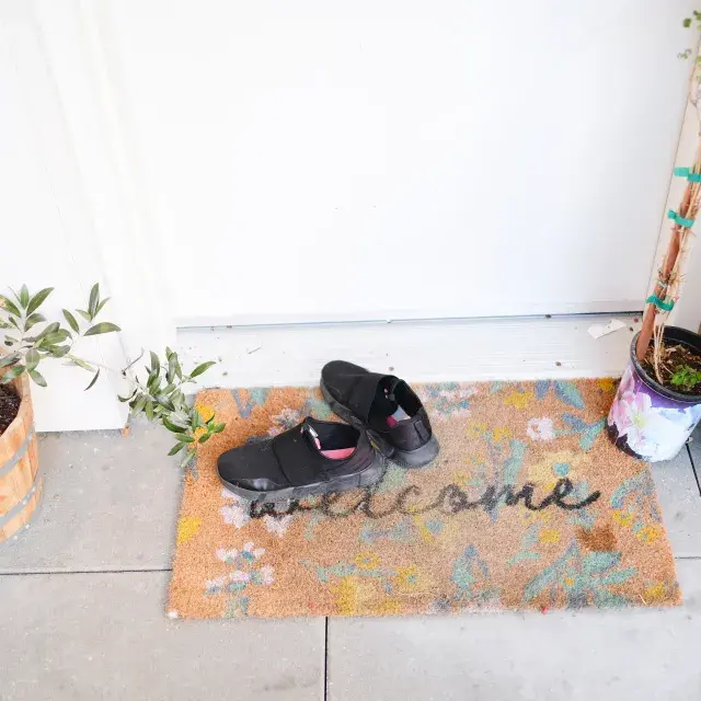 A welcome mat with shoes in front of a doorway with flower pots on both sides
