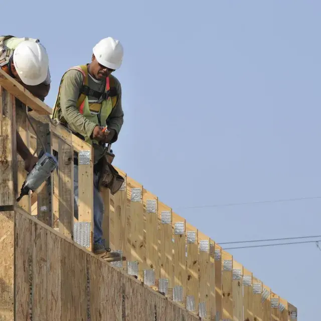 Two construction workers framing a roof on new housing