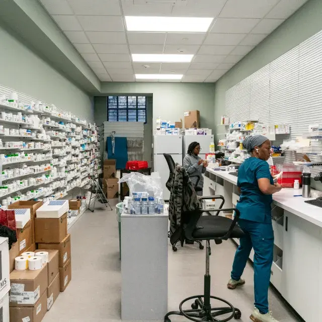 Two women working at computers in a fully stocked pharmacy.