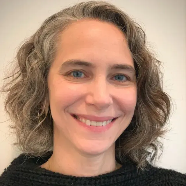 Person with short wavy salt and pepper hair smiles
