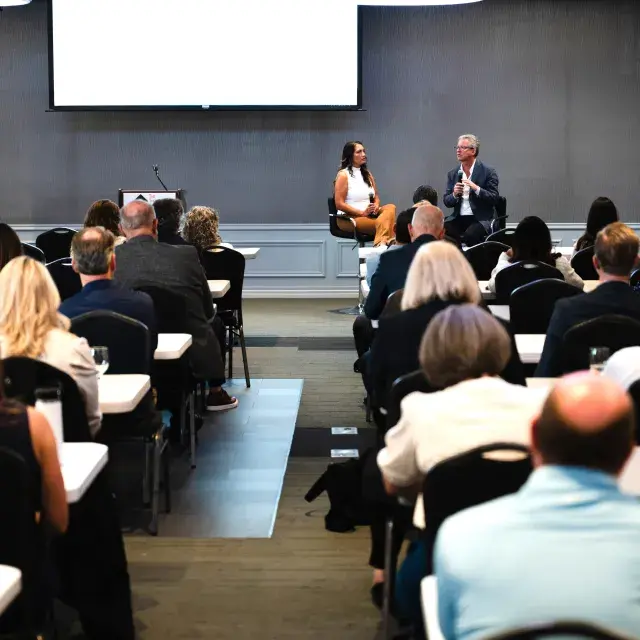 Two people seated at front of room talking with audience before them