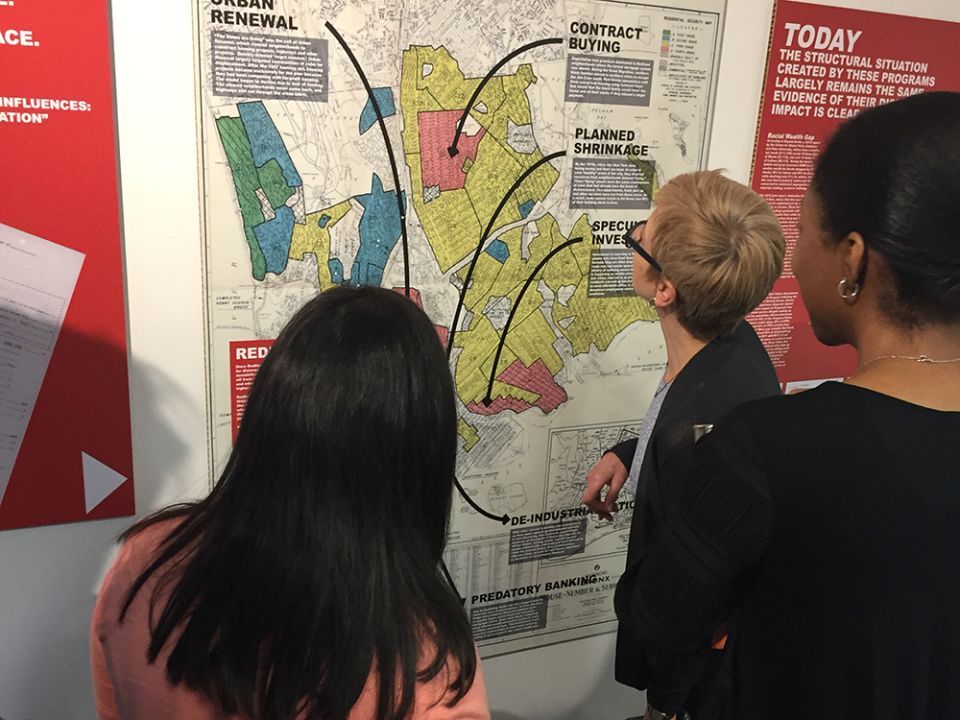 Three woman looking at the Undesign the Redline exhibit