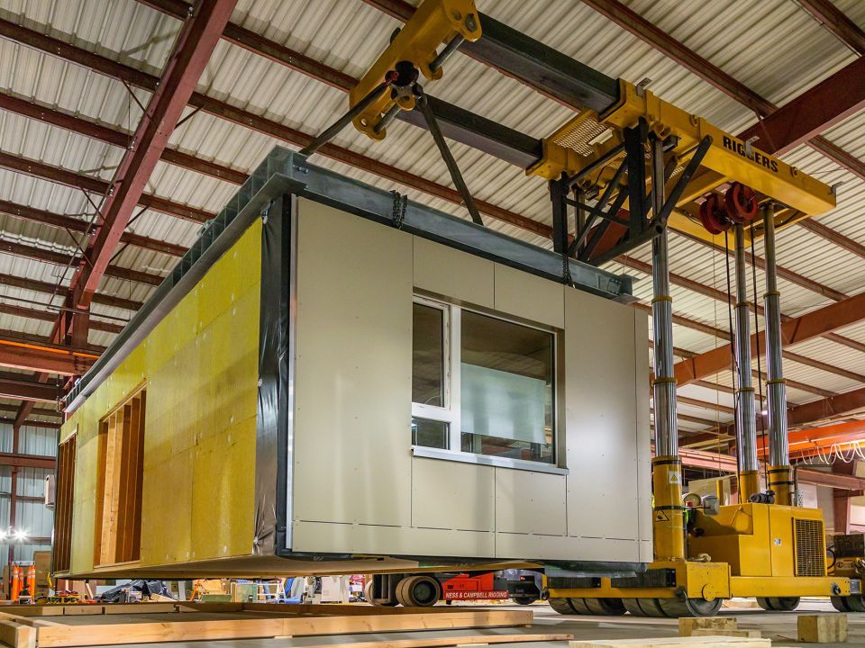 A prefabricated room being built and lifted inside a warehouse