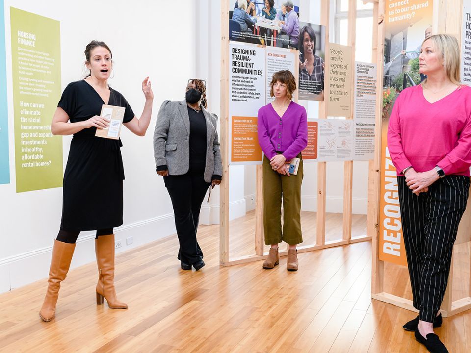 A woman presenting on the exhibit while three other women watch and listen