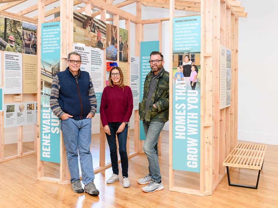 Three people standing in front of the exhibit smiling and posing for a picture