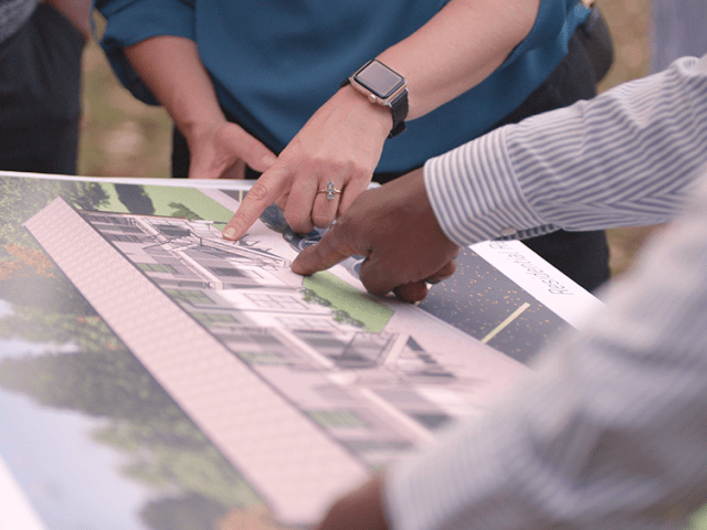 The hands of two people pointing at a picture.